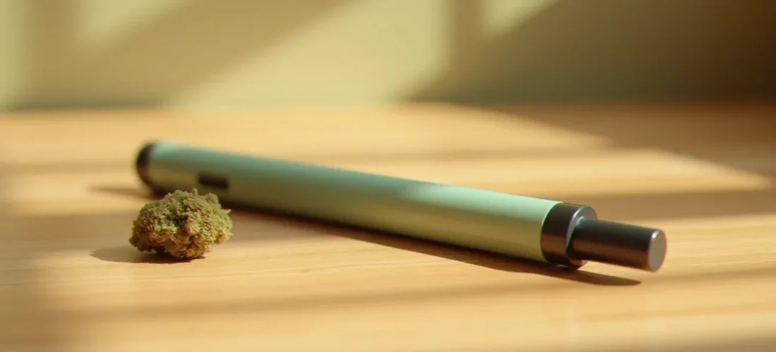 Puff CBD pastel posée sur une surface en bois naturel avec une fleur de chanvre séchée, photographie produit professionnelle en lumière naturelle